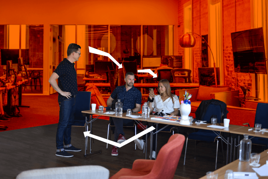 A group of people having a discussion, one is standing and two are sitting behind a desk