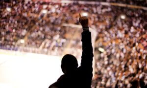 Picture taken of fans sitting in their seats inside a stadium, one man in the center of the picture celebrating