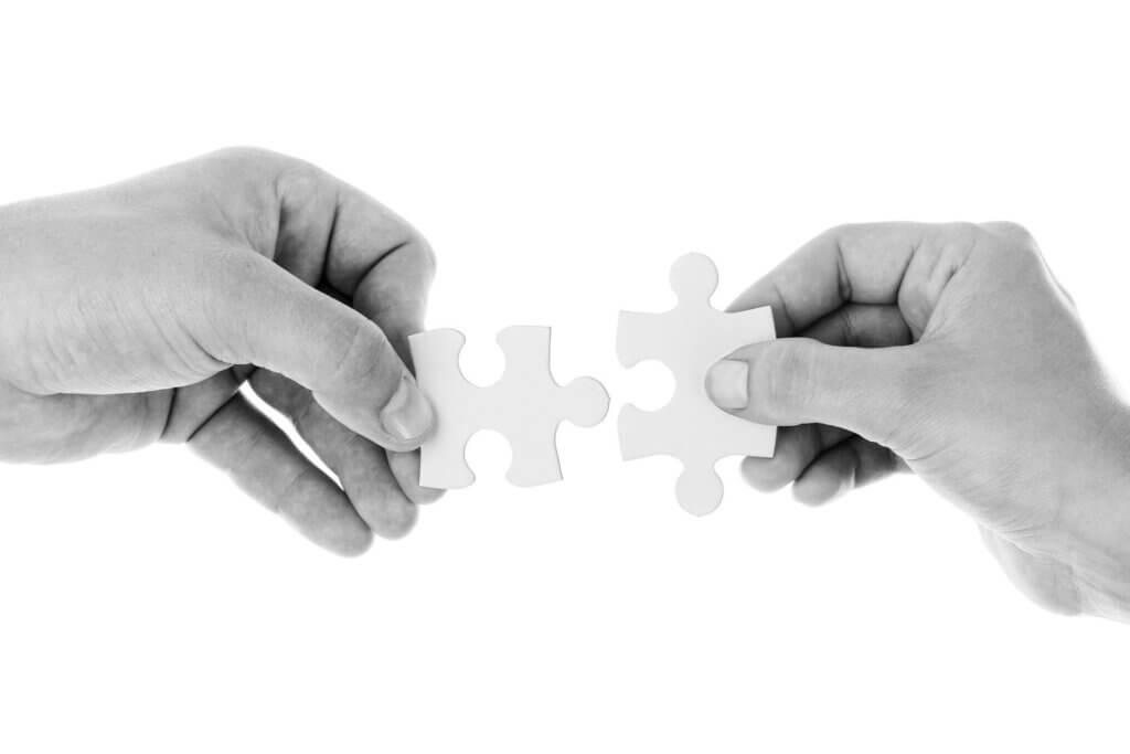 Black and white picture of two hands, each holding a puzzle piece