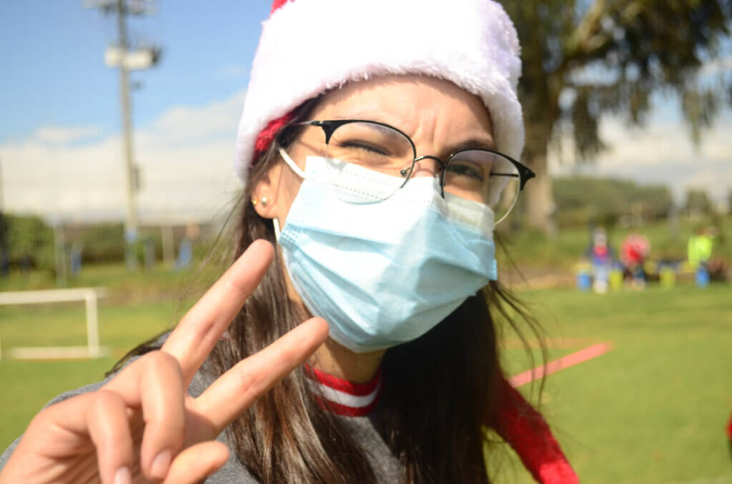 Girl doing the peace sign while wearing glasses, facemask and a santa hat