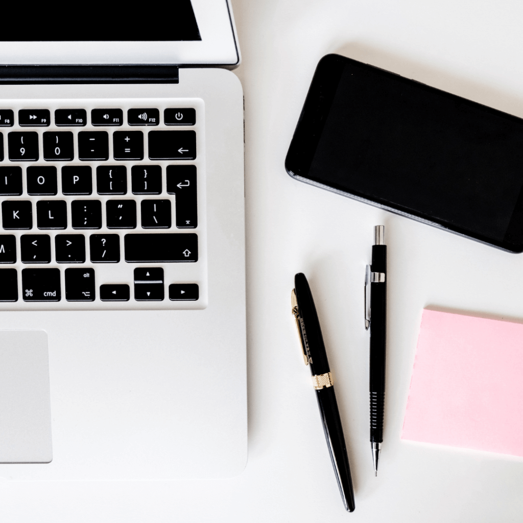 a laptop on a desk with two pens, a phone and post it notes next to it