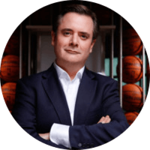 1518529290228 Middle aged, serious looking man in a suit standing with his arms corssed in front off basketballs, he's looking into the camera