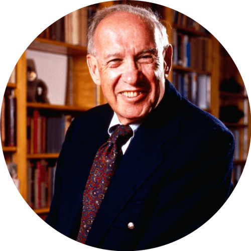 Old man in a library wearing a suit, smiling while looking into the camera